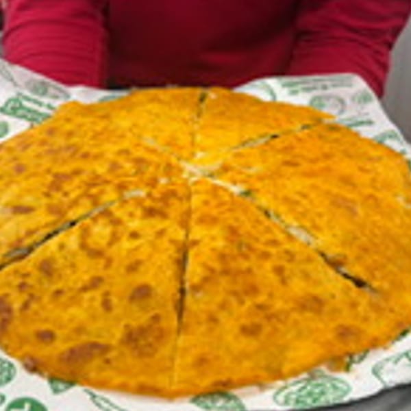 A large, round, golden-brown quesadilla from Taco Riendo Taqueria, sliced into wedges on a paper liner.