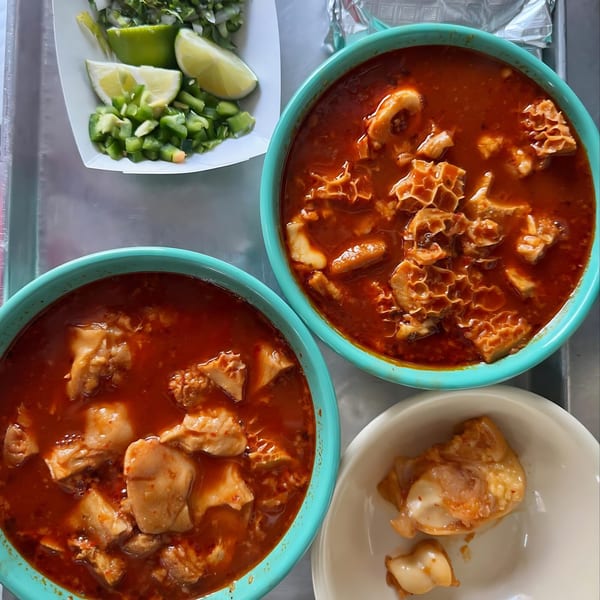 Two bowls of menudo soup with tripe, served with a side of chopped onions, jalapeños, and lime wedges.