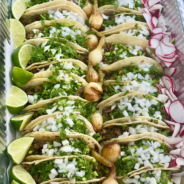 Rows of Tacos Riendo Taqueria tacos with onions, cilantro, limes, radishes, and grilled onions.