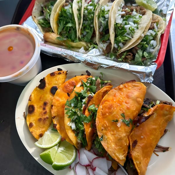 Plates of birria tacos and regular tacos with cilantro, onions, lime, and a side of consommé.