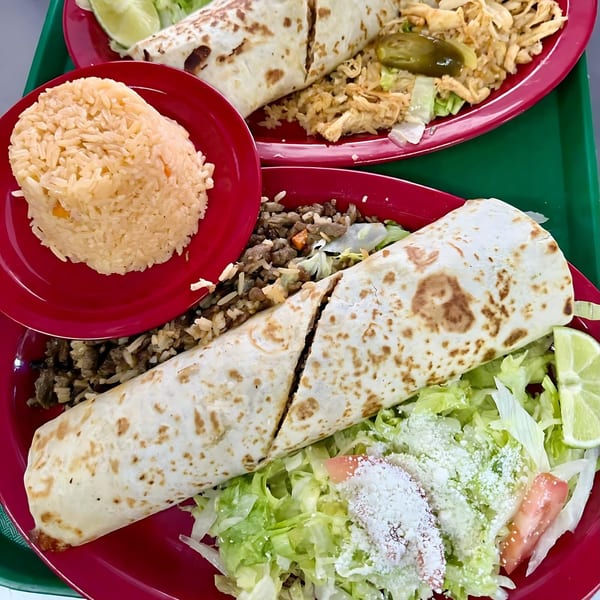 Two burritos on red plates, one with rice and meat, the other with rice and chicken.