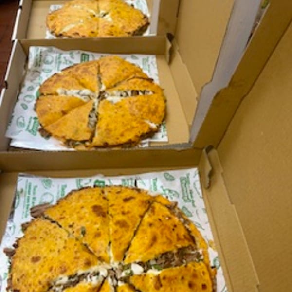 Three large, round quesadillas, cut into wedges, in cardboard takeout boxes from Taco Riendo Taqueria.