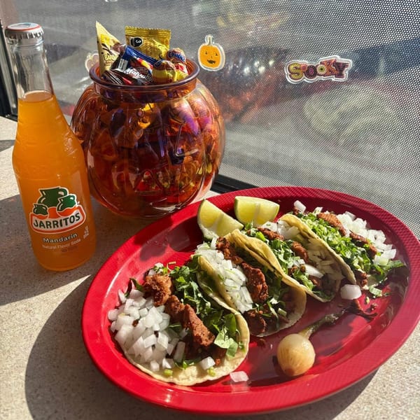 Three tacos with meat, onions, and cilantro on a red plate with a Jarritos soda and candy.