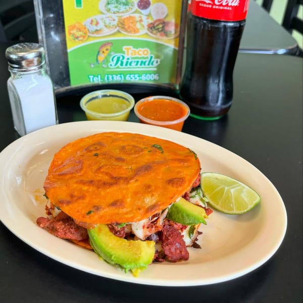 A Taco Riendo quesadilla with avocado and lime, with sauces, salt, and a soda in the background.