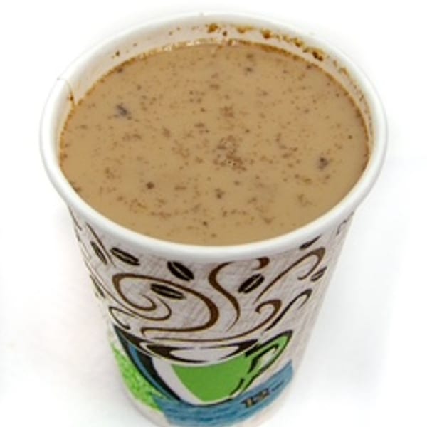 A paper cup filled with a light brown beverage, possibly coffee or champurrado, with small dark specks.