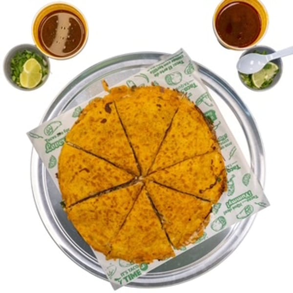 A large, round quesadilla cut into eight slices on a metal tray with two cups of consommé.