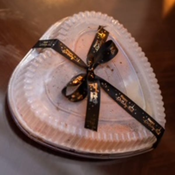 Heart-shaped dessert in a clear plastic container, tied with a black and gold ribbon.
